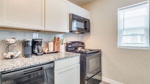 A modern kitchen with white cabinets, a stainless steel microwave, a coffee maker, and a stove. - Walking Distance to Downtown Wichita | In Unit W/D (Wichita)