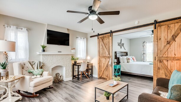 A living room with a fireplace, a ceiling fan, a TV, and a sliding barn door leading to a bedroom. - Walking Distance to Downtown Wichita | In Unit W/D (Wichita)