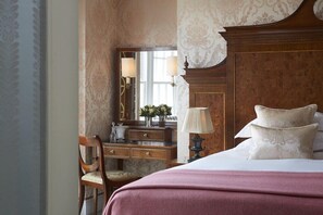 A hotel room with a wooden headboard, a bedside table with a lamp, a mirror, and a dresser with a mirror.