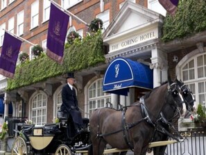 A horse-drawn carriage in front of The Goring Hotel, with a traditional building facade and a blue awning.