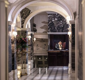 A formal interior with a marble floor, a reception desk, and a wall with a tree mural. - The Goring (London)