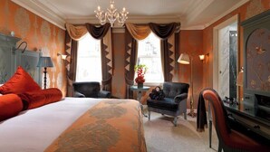 A hotel room with a large bed, two armchairs, a desk, and a chandelier. - The Goring (London)