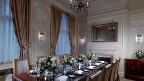 Una sala da pranzo formale con un lungo tavolo apparecchiato per un pasto, affiancato da sedie, un lampadario e un camino.