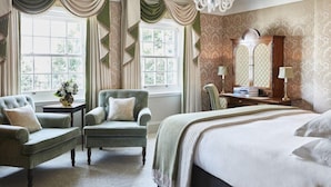 A bedroom with a large bed, two armchairs, a nightstand, a dresser, and a mirror. - Goring Hotel (London)
