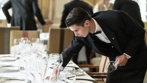 A formal dining setting with a waiter attending to a table set with multiple wine glasses and plates. - Goring Hotel (London)