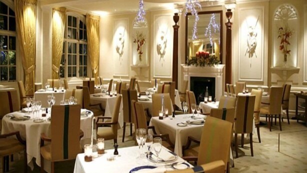 A formal dining room with tables set for multiple guests, elegant chairs, and a fireplace. - The Goring (London)