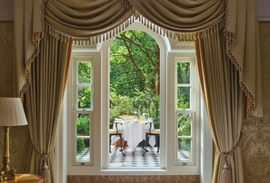 A room with a large arched window, curtains, a table set for breakfast, and a lamp. - The Goring (London)