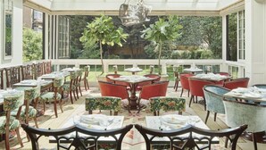 A sunlit dining area with tables and chairs, a central round table, and a view of greenery outside. - Goring Hotel (London)