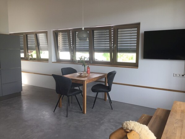 A modern dining area with a wooden table, four chairs, and a TV mounted on the wall.
