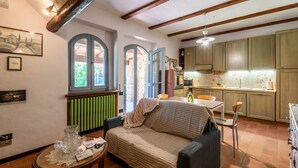 A cozy living room with a sofa, a table with a glass centerpiece, and a kitchen area with wooden cabinets and a radiator. - "Volpe" Apartment with Pool Reserved for Guests, Wi-Fi, and Air Conditioning (San Gimignano)
