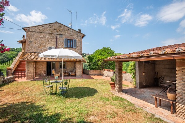 Una casa de piedra con patio, mobiliario exterior y un espacio cubierto.