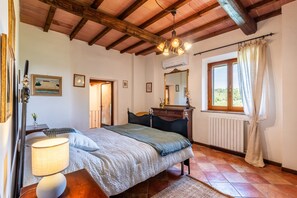 Un dormitorio con cama, mesita de noche, lámpara, cómoda, espejo, ventana con cortinas y radiador.