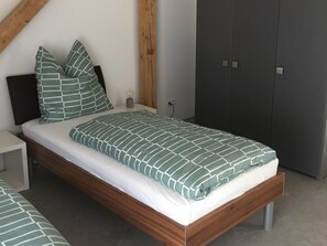 A bedroom with a wooden bed frame, a grey wardrobe, and a bedside table.