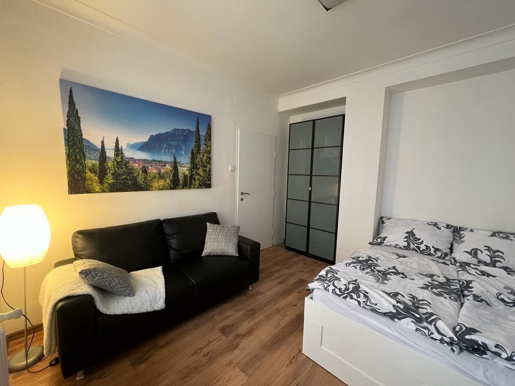 Et soveværelse med en seng, en sort lædersofa, et billede hængt på væggen og en gulvlampe.