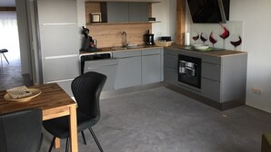 A modern kitchen with grey cabinets, a wooden countertop, a black chair, and a dining table.