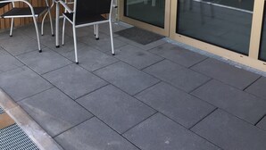 An outdoor seating area with a table and chairs, a sliding glass door, and a wooden wall.