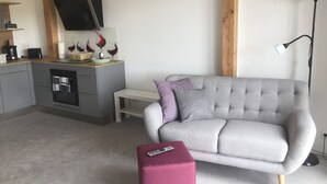 A modern living room with a grey sofa, a small white table, and a pink ottoman.