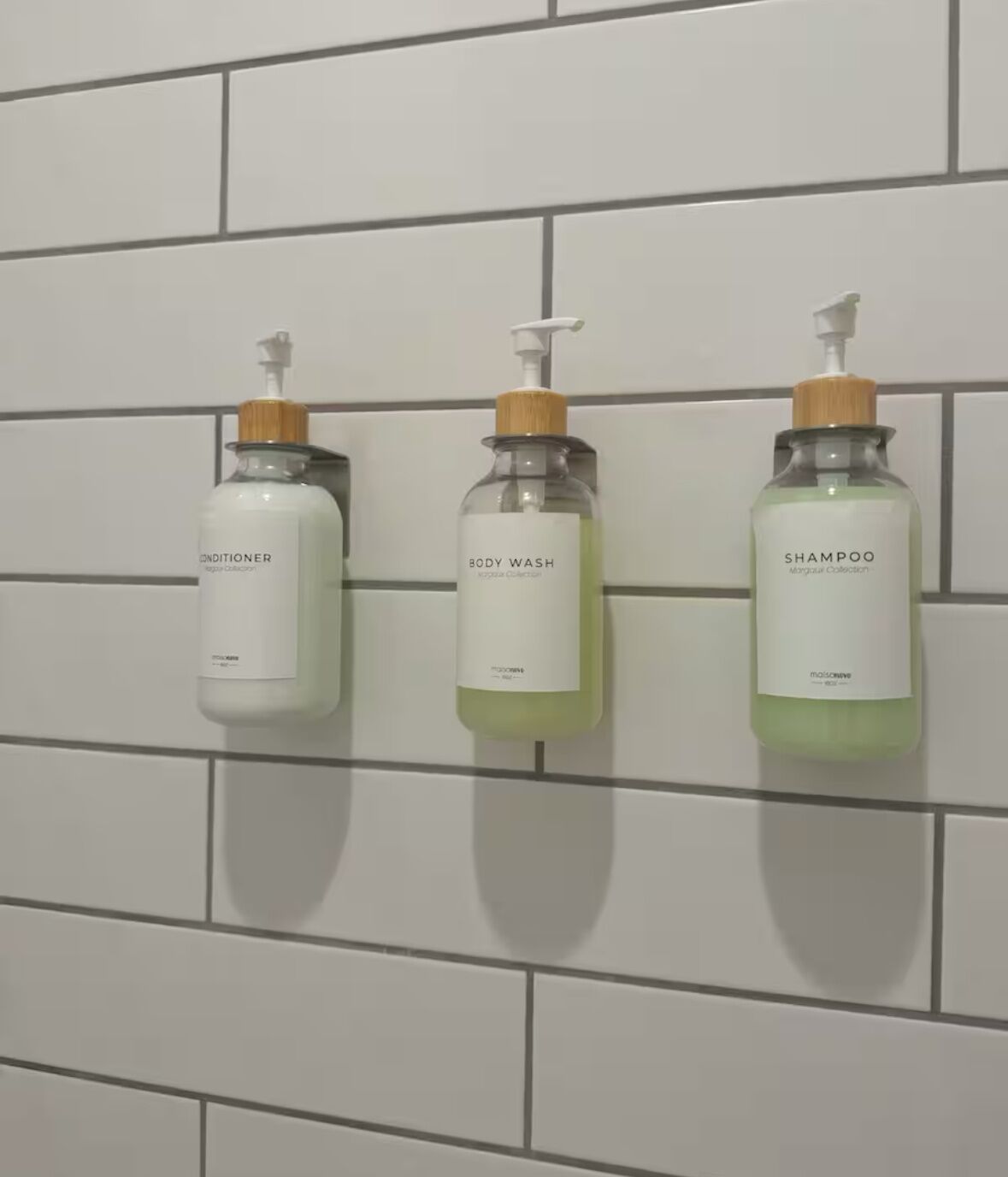 Trois bouteilles de gel douche, d’après-shampoing et de shampoing sont suspendues à un mur carrelé.
