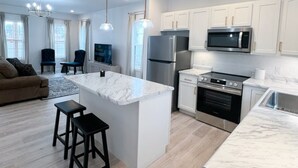 A modern kitchen with white cabinets, stainless steel appliances, and a marble island. - Cottage 4 at MeadowView- near cave run lake! (Morehead)