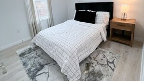 A bedroom with a bed, a nightstand, a lamp, a window with curtains, and a ceiling light. - Cottage 4 at MeadowView- near cave run lake! (Morehead)