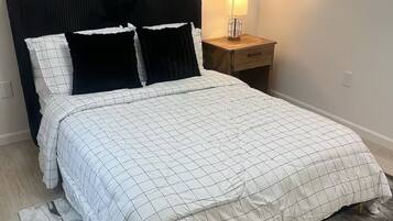 Een net opgemaakt bed met een zwart-wit geruit dekbed, een zwart hoofdbord en een bedlampje op een houten nachtkastje.