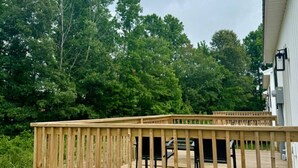 A wooden deck with a railing, a black chair, and a building in the background. - Cottage 4 at MeadowView- near cave run lake! (Morehead)