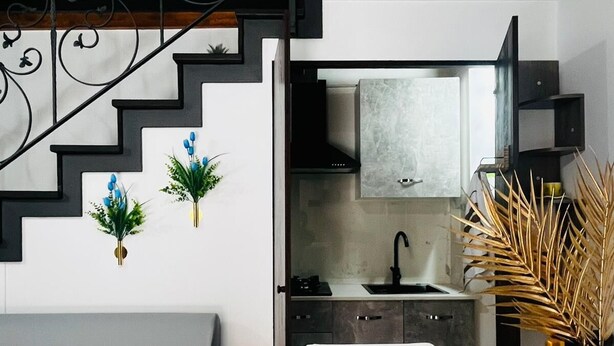 A modern kitchen with a built-in stove, a white sink, and a black range hood. There is a staircase with black railings leading to an upper level. - Giupa's home (Catania)