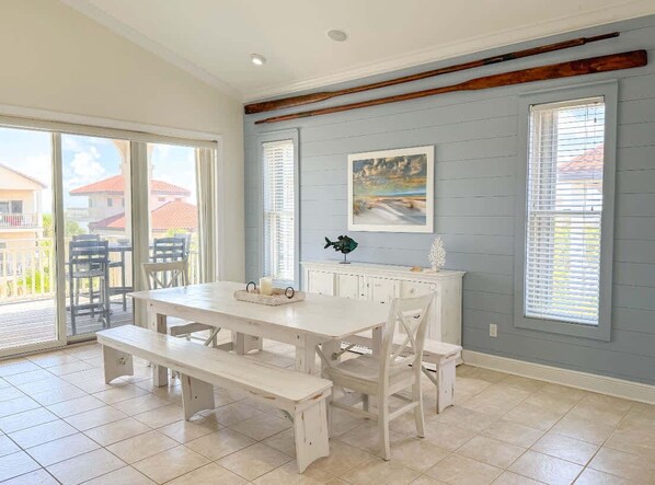 Un coin repas avec une table et des bancs blancs, un meuble blanc agrémenté d’objets décoratifs et un tableau au mur.