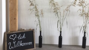 Ein Zimmer mit sichtbarem Holzbalken, drei Blumentöpfen und einem Willkommensschild.