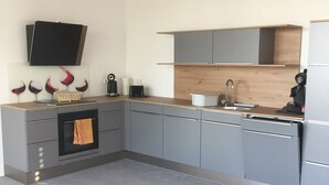 Eine moderne Küche mit grauen Schränken, einem Backofen, einem Spülbecken und einem Flachbildfernseher, der über der Arbeitsplatte angebracht ist.