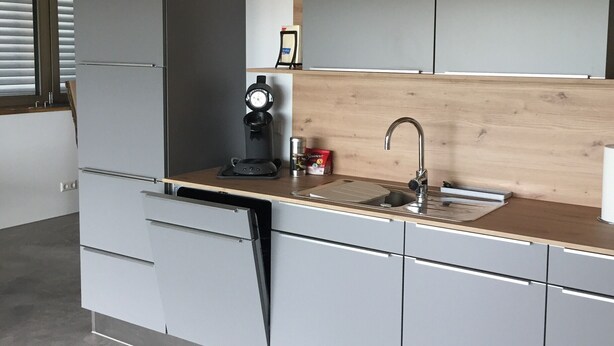 Eine moderne Küche mit grauen Schränken, einer Holz Arbeitsplatte, einer Spüle und einer Kaffeemaschine.