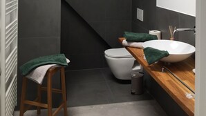 Ein modernes Badezimmer mit Holzbalkendecke, einer weißen Toilette, einem Holzwaschtisch mit weißem Waschbecken und einem grünen Handtuch auf dem Hocker.