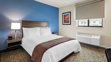 Quarto de hotel com cama, mesa de cabeceira, luminária, janela com vista e ar condicionado.