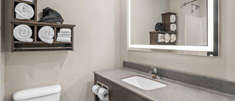 A bathroom with a toilet, a sink, a mirror, and a shelf with towels.