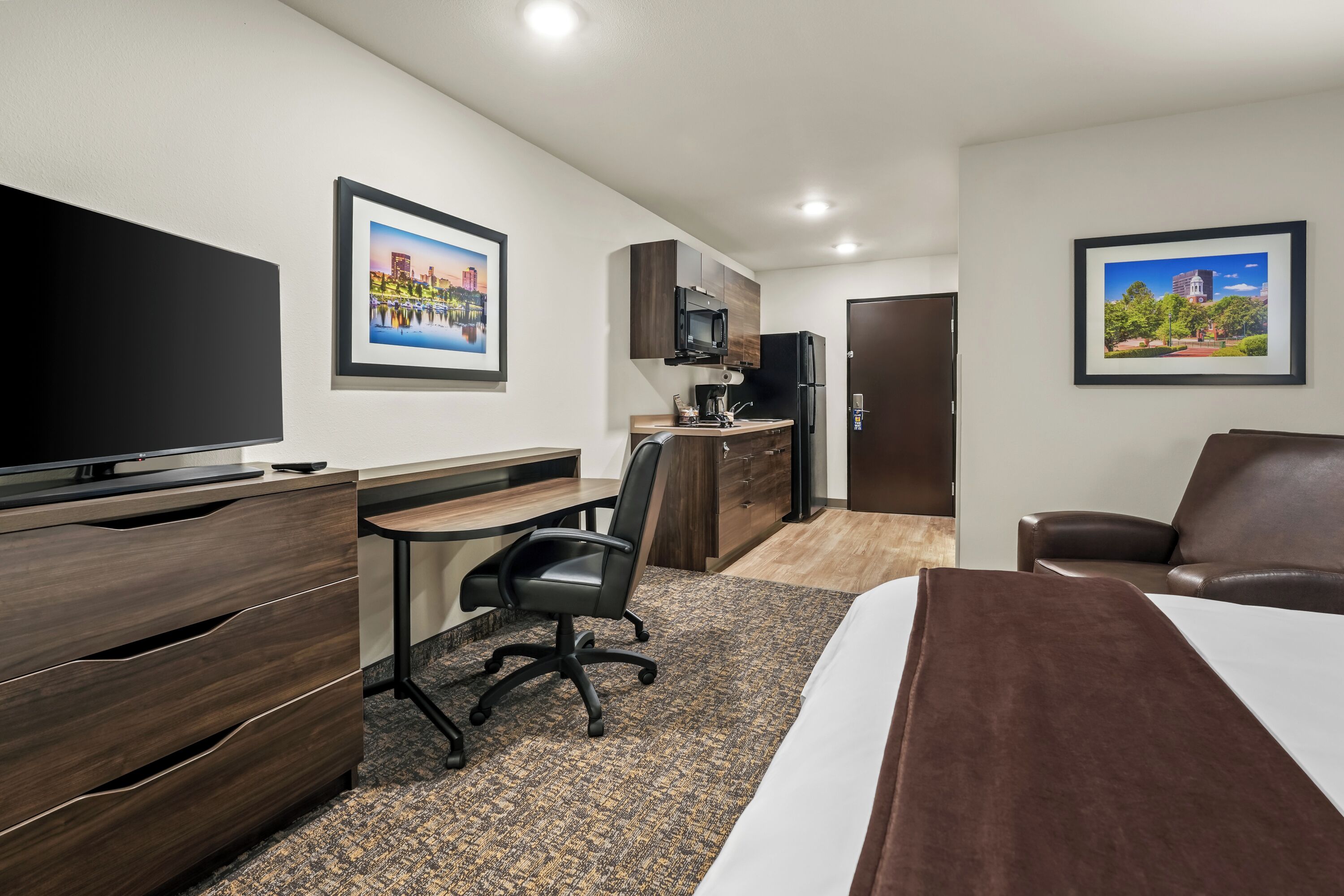 A hotel room with a bed, a desk, a chair, a TV, a microwave, and a refrigerator.