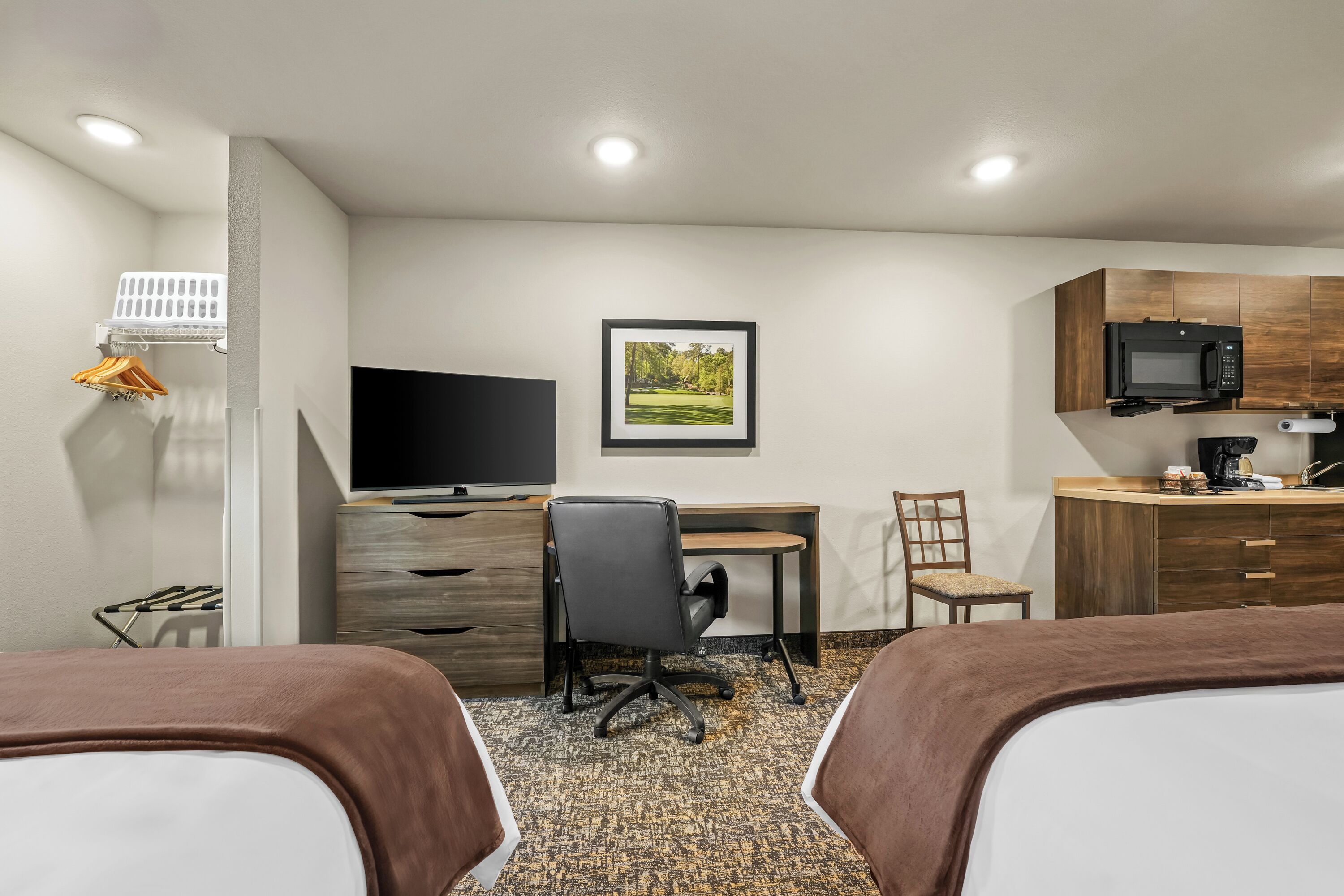 A hotel room with two beds, a desk, a chair, a television, a microwave, and a small kitchen area.