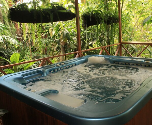 Een kuip met warm water, een houten rand en uitzicht op weelderige begroeiing.