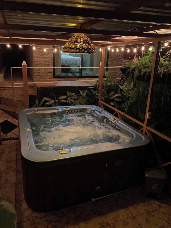 A hot tub with a wooden deck and string lights, surrounded by plants and a brick wall. - Cabaña Luculuc Garden & Forest (La Tigra)