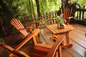 A wooden deck with Adirondack chairs and a table, surrounded by a wooden fence and lush greenery. - Cabaña Luculuc Garden & Forest (La Tigra)