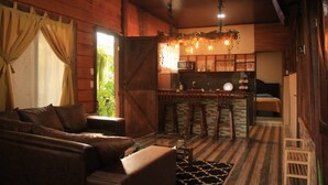 Une chambre confortable de style cabane, avec un intérieur en bois, un canapé, une table basse en verre, un coin cuisine avec un bar et un lit.