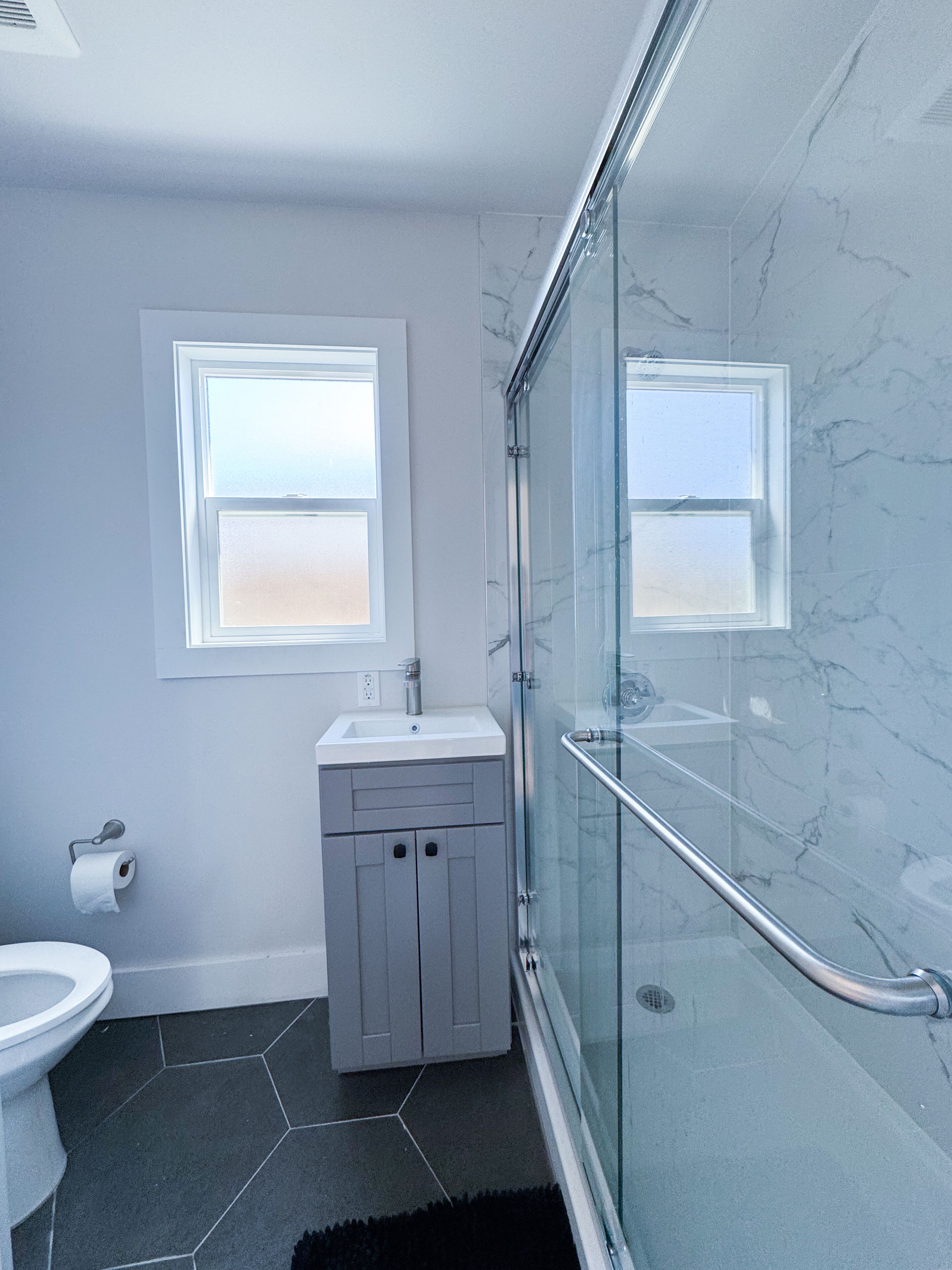 A modern bathroom with a glass shower enclosure, a toilet, and a sink with a marble countertop.