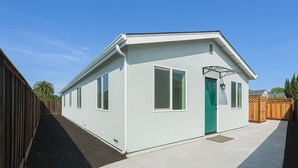 A small, single-story building with a light-colored exterior, a green door, and a small porch area. - New Build Smart Home 3 Bedroom (Sunnyvale)