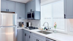 A modern kitchen with grey cabinets, stainless steel appliances, and a large window with blinds. - New Build Smart Home 3 Bedroom (Sunnyvale)