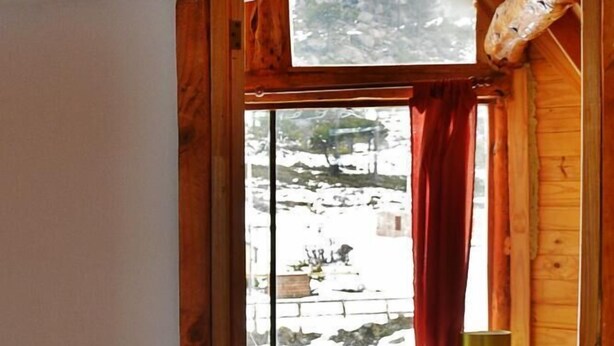 Habitación de una cabaña de madera con cama, ventana que ofrece vistas a un paisaje nevado y una mesita con una lámpara.