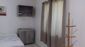 A bedroom with a bed, a wardrobe, a shelf with hangers, and a curtain. - Pousada Belezinha (Arraial do Cabo)
