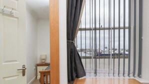 Una stanza con un comò in legno, un tavolino con una lampada e vista su un porto turistico attraverso finestre con sbarre.