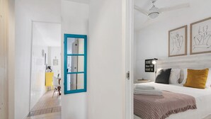 Una camera da letto con un letto, un comodino, una finestra con cornice blu e un quadro appeso al muro.