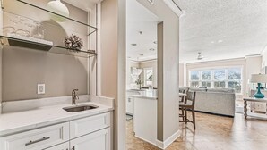 Une cuisine moderne dotée d’un évier encastré, de meubles blancs et d’une étagère en verre où sont disposés des verres à vin.