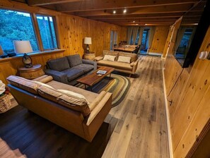 L’intérieur chaleureux d’un chalet, avec des murs et des planchers en bois, comprenant un canapé, une table à manger et une lampe.