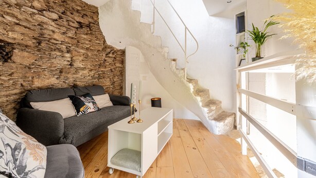 A living room with a stone wall, a staircase, a sofa, a white side table, and a potted plant. - Holiday Home 'Le Moulin De Pen Hoêt' with Shared Garden (Vertou)